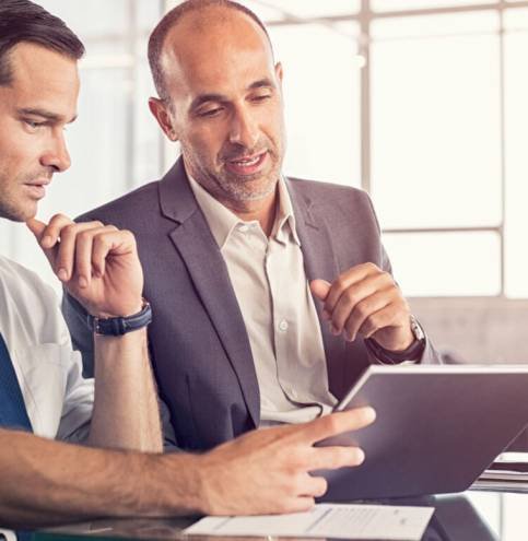 Businessman using a digital tablet to discuss information with senior leadership in a meeting. Business partners discussing plans. Mature boss and young business man working together in office.